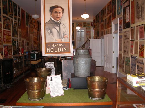Interior of a museum featuring Harry Houdini memorabilia, with posters on the walls and vintage props displayed.