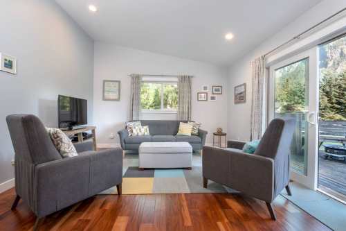 Cozy living room with two armchairs, a sofa, and a coffee table, featuring large windows and wooden flooring.