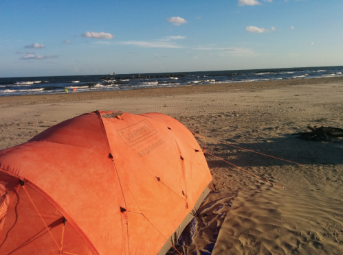 An orange tent on a sandy beach with gentle waves and a clear blue sky in the background.
