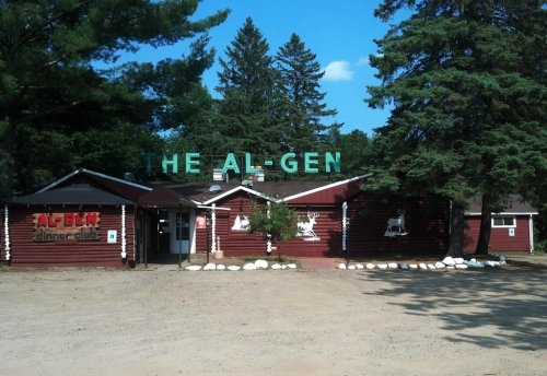 A rustic building with a sign reading "THE AL-GEN" surrounded by trees and a gravel path.