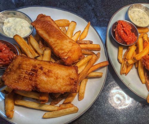 Two plates of golden-brown fish and chips, served with dipping sauces on the side.