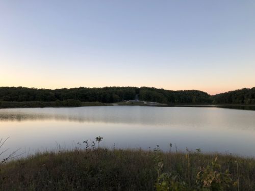 A serene lake surrounded by trees at dusk, reflecting the soft colors of the sky.