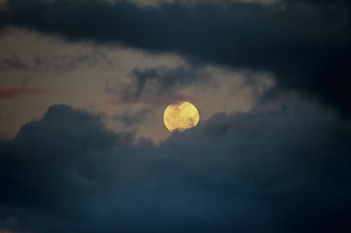 A full moon partially obscured by dark clouds against a twilight sky.
