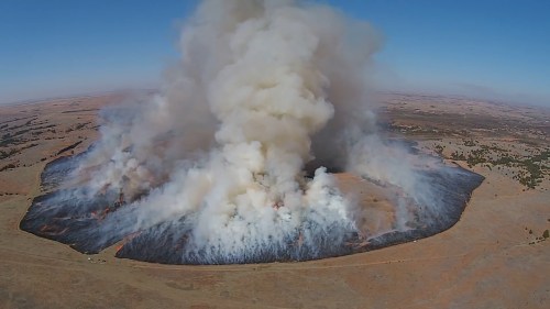 Aerial view of a large wildfire producing thick smoke over a scorched landscape.