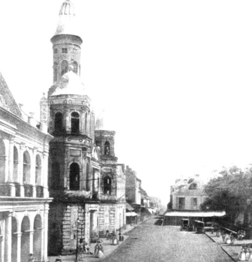 Historic street scene featuring old buildings and a tower, with people and horse-drawn carriages visible.