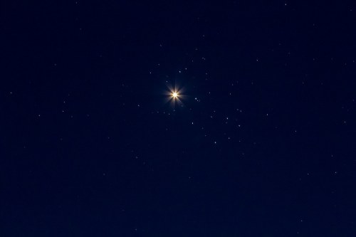 A bright star shines in a dark night sky filled with scattered stars.