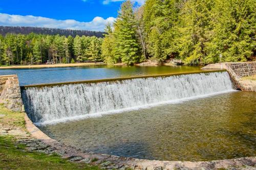 A serene landscape featuring a waterfall cascading over a stone dam into a calm lake, surrounded by lush green trees.