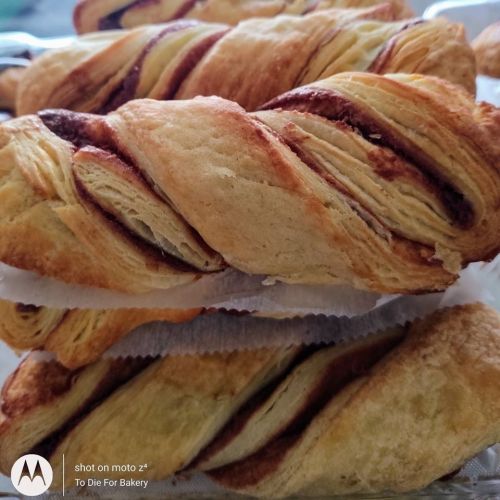Freshly baked twisted pastries with a golden-brown crust and chocolate filling, stacked on parchment paper.