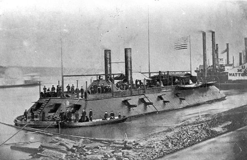Historic black-and-white photo of a steam-powered riverboat docked, with crew members on board and nearby boats.