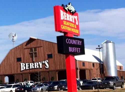 Sign for Berry's Seafood & Catfish House in front of a large barn-style building with a silo and parked cars.