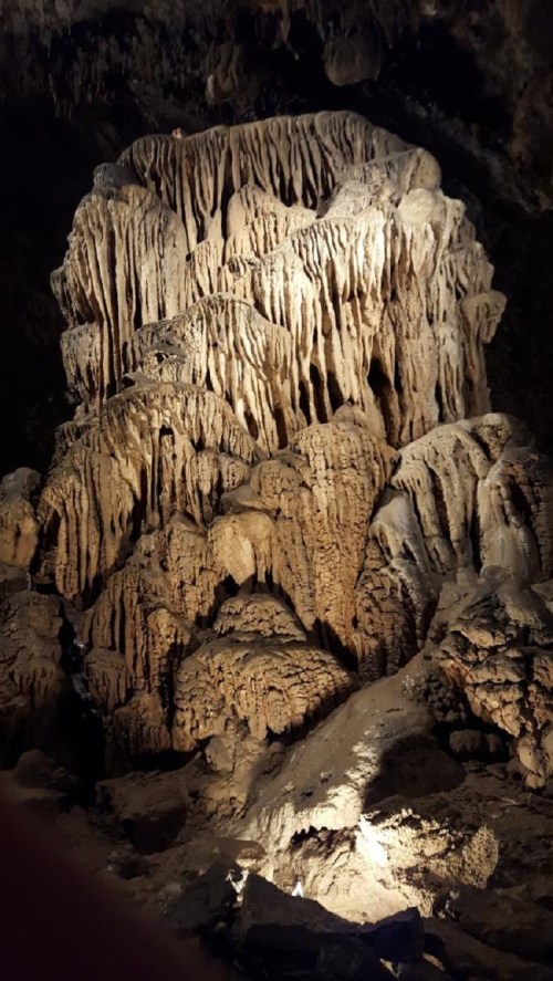 A well-lit cave formation with intricate, textured stalagmites and stalactites, showcasing natural geological patterns.