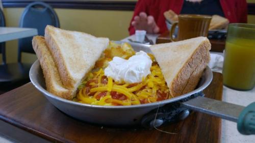 A skillet filled with cheesy hash browns topped with sour cream, served with two slices of toast on the side.