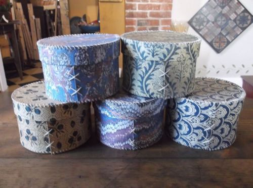 A stack of decorative, patterned boxes with stitched edges, arranged on a wooden surface.