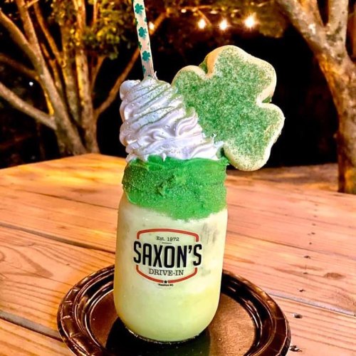 A festive green milkshake topped with whipped cream and a shamrock cookie, served in a jar with a straw.