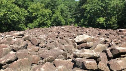 A rocky landscape covered with large boulders, surrounded by lush green trees and foliage.