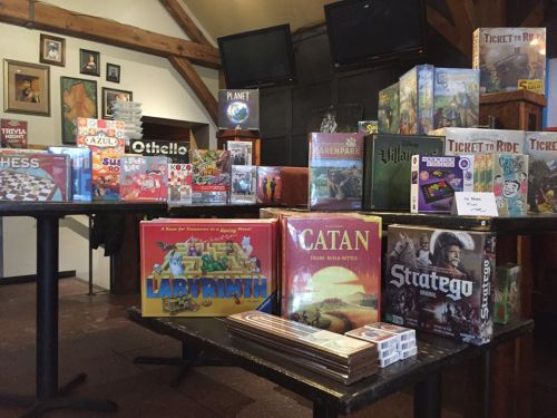 A display of various board games on tables, including Catan, Ticket to Ride, and Labyrinth, in a cozy setting.