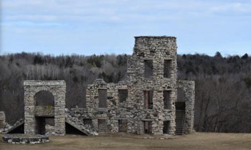 Stone ruins of a historic building surrounded by trees under a cloudy sky.