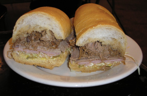 A close-up of a sandwich filled with sliced beef, ham, and lettuce, served in a soft, crusty bread roll.