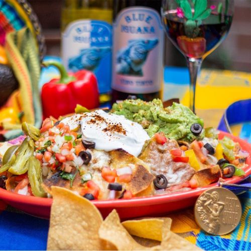 A vibrant plate of nachos topped with guacamole, sour cream, and fresh salsa, alongside chips and drinks.