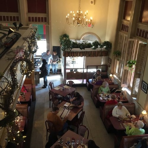 A cozy restaurant interior with booths, tables, and patrons dining, featuring warm lighting and festive decorations.