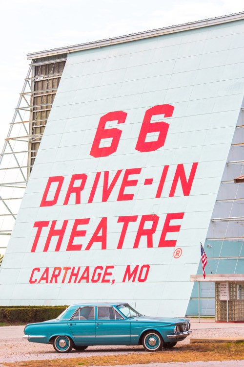 A vintage car parked in front of the 66 Drive-In Theatre sign in Carthage, Missouri.