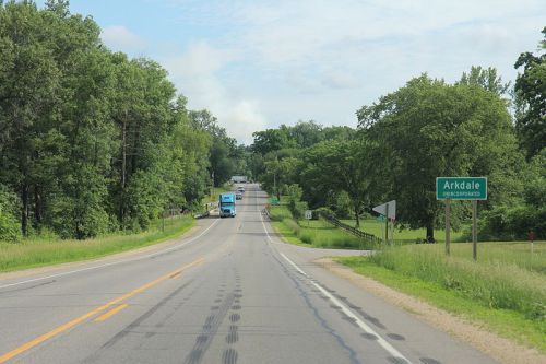 A rural road leads to Arkdale, lined with trees and a sign indicating the town ahead.