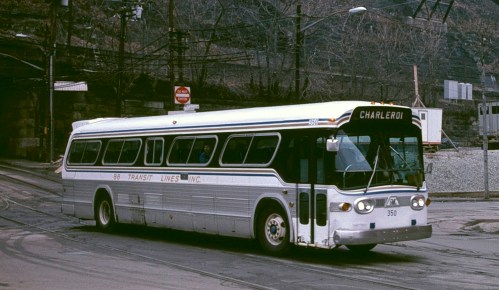 A vintage bus labeled "Charleroi" from 88 Transit Lines, driving on a city street with a hilly background.