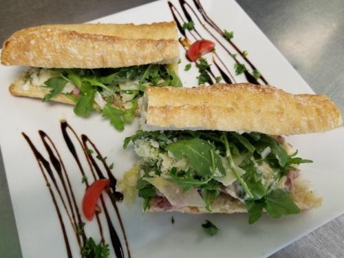 Two sandwiches on a white plate, filled with greens and cheese, drizzled with balsamic and garnished with herbs and tomatoes.