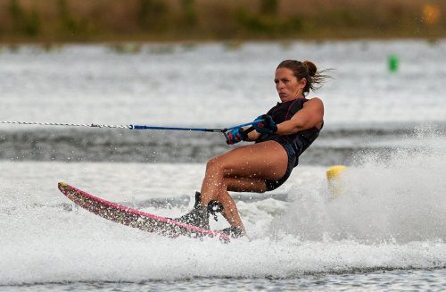 A woman water skiing on a lake, skillfully navigating the water with splashes around her.