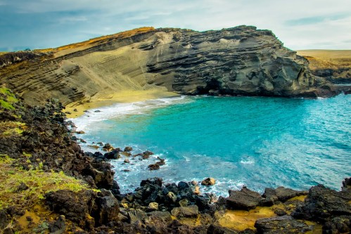A scenic view of a rocky coastline with turquoise waters and a sandy beach, surrounded by rugged cliffs.