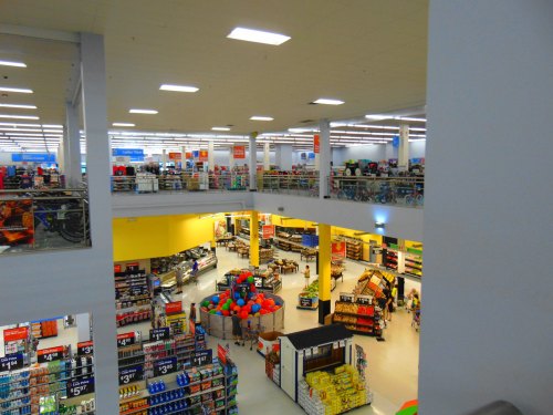 A spacious retail store interior with multiple aisles, shelves stocked with products, and shoppers browsing.