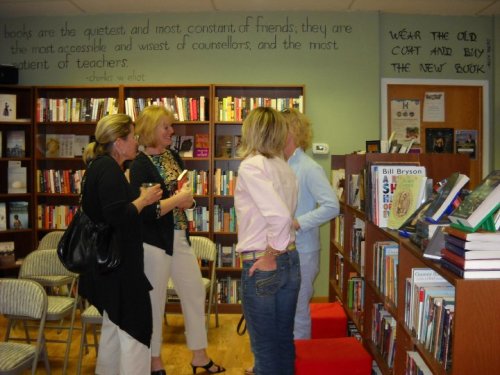 Four women browse books in a cozy bookstore, surrounded by shelves filled with various titles.