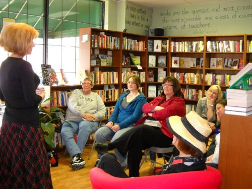 A group of people attentively listening to a speaker in a cozy bookstore filled with books and shelves.