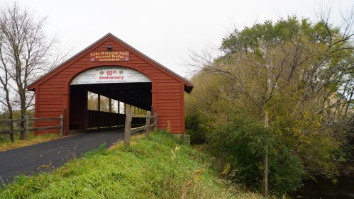 A red covered bridge over a path, surrounded by trees and greenery, with a sign celebrating a 10th anniversary.