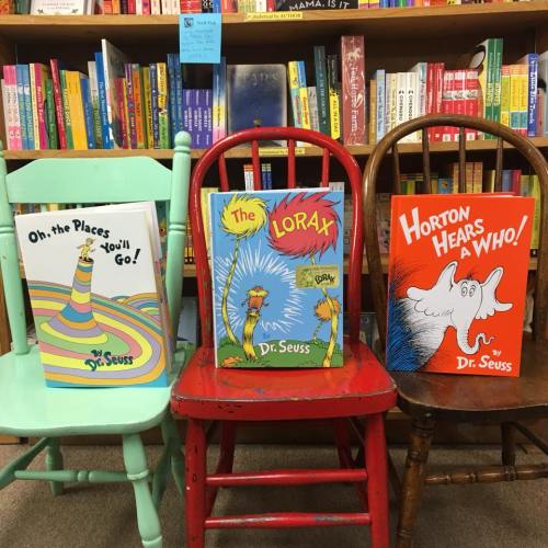 Three colorful children's books by Dr. Seuss displayed on chairs in a bookstore: "Oh, the Places You'll Go!", "The Lorax", and "Horton Hears a Who!".