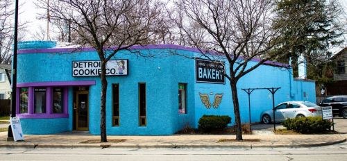 Bright blue bakery building with purple trim, featuring signs for "Detroit Cookie Co." and "Bakery," surrounded by trees.