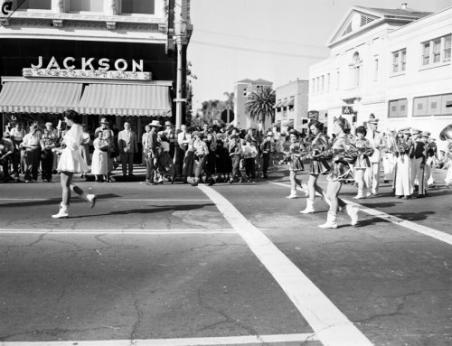 A parade scene with a marching band and performers, crowds watching near a restaurant named Jackson.