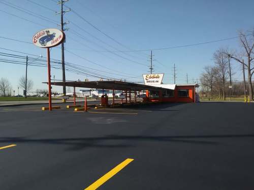 A retro drive-in restaurant with a bright orange exterior and a covered carport, set against a clear blue sky.