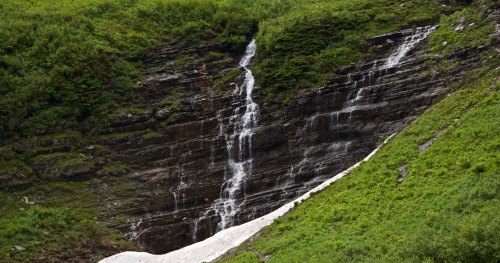 A cascading waterfall flows down a rocky cliff, surrounded by lush green vegetation.
