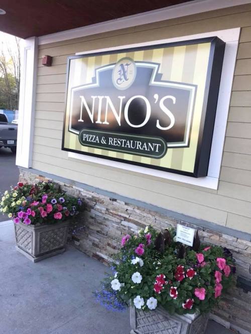 Sign for Nino's Pizza & Restaurant with colorful flower planters in front.