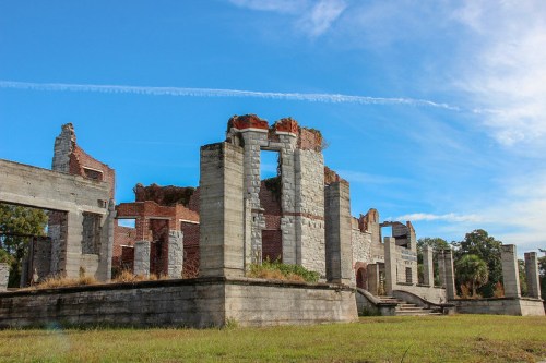 Ruins of a stone and brick building with partially collapsed walls, set against a blue sky with wispy clouds.