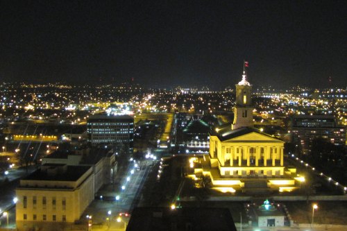 A nighttime view of a city skyline featuring a lit-up government building and twinkling city lights.
