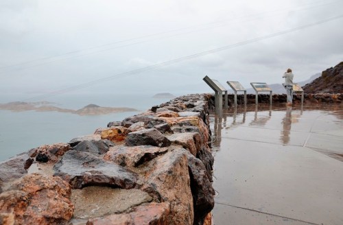 A rocky viewpoint overlooking a misty landscape, with informational signs and a person standing in the distance.