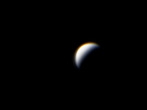 A distant view of a planet's curved surface illuminated by sunlight against a black background.