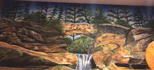 A vibrant mural depicting a stone bridge over a waterfall, surrounded by lush trees and rocky terrain.