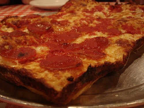A close-up of a rectangular pizza topped with pepperoni and melted cheese, resting on a silver platter.