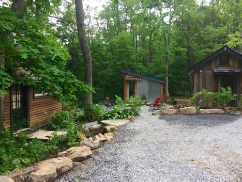 Two small cabins nestled in a lush green forest, surrounded by gravel paths and natural landscaping.