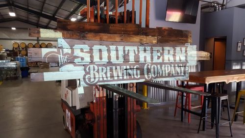 Sign for Southern Brewing Company made of wooden planks, displayed in a brewery setting with barrels in the background.