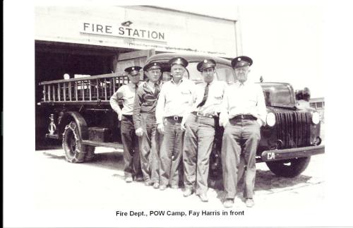 Black and white photo of five men in uniforms standing in front of a fire station with a vintage fire truck.