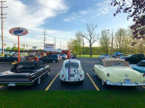 Three classic cars parked outside a diner, with a clear sky and trees in the background.